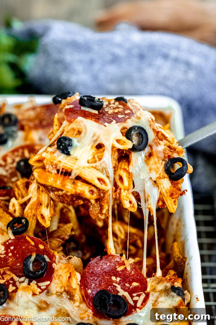Our deliciously hearty pizza casserole will be kids of all ages will race to the dinner table when this is on the menu! Ooey-gooey, cheese YUM! #pizzacasserole #pizzapastacasserole scooping pizza pasta casserole