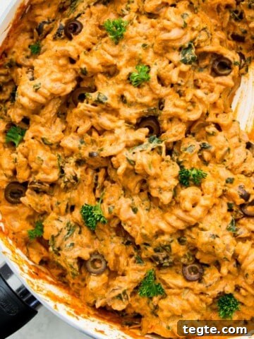 A pan filled with vegan sun-dried tomato pasta with a serving spoon in it.