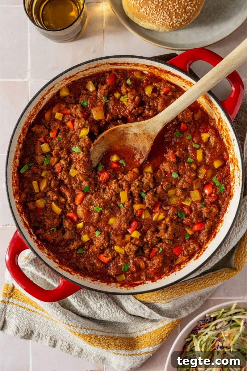 Lean Ground Beef Sloppy Joes with Tangy Tomato Sauce 10 A pan with a tomato sauce and ground beef mixture in it with a wooden spoon in the sauce.