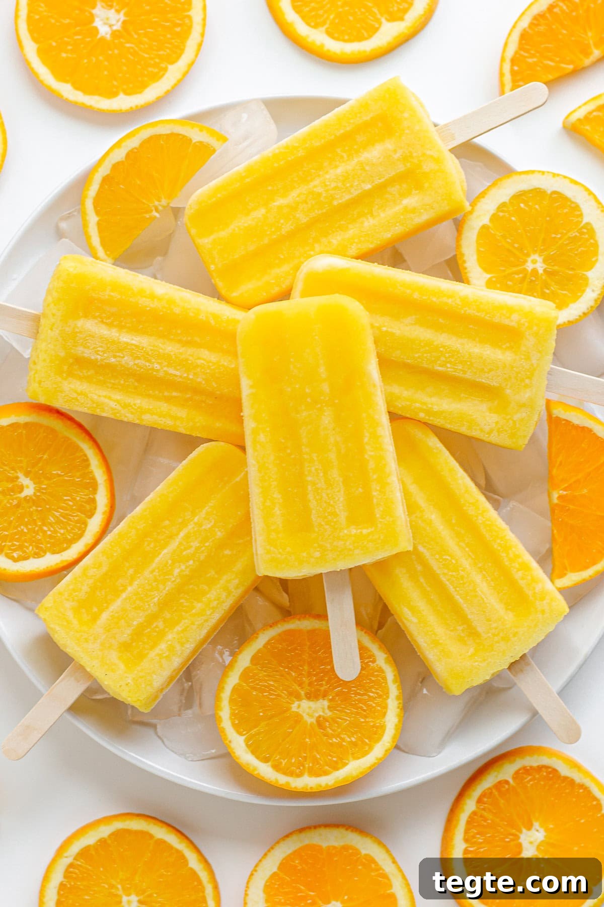 Refreshing Homemade Orange Popsicles Recipe 2 Orange popsicles piled on a plate of ice surrounded by orange slices.