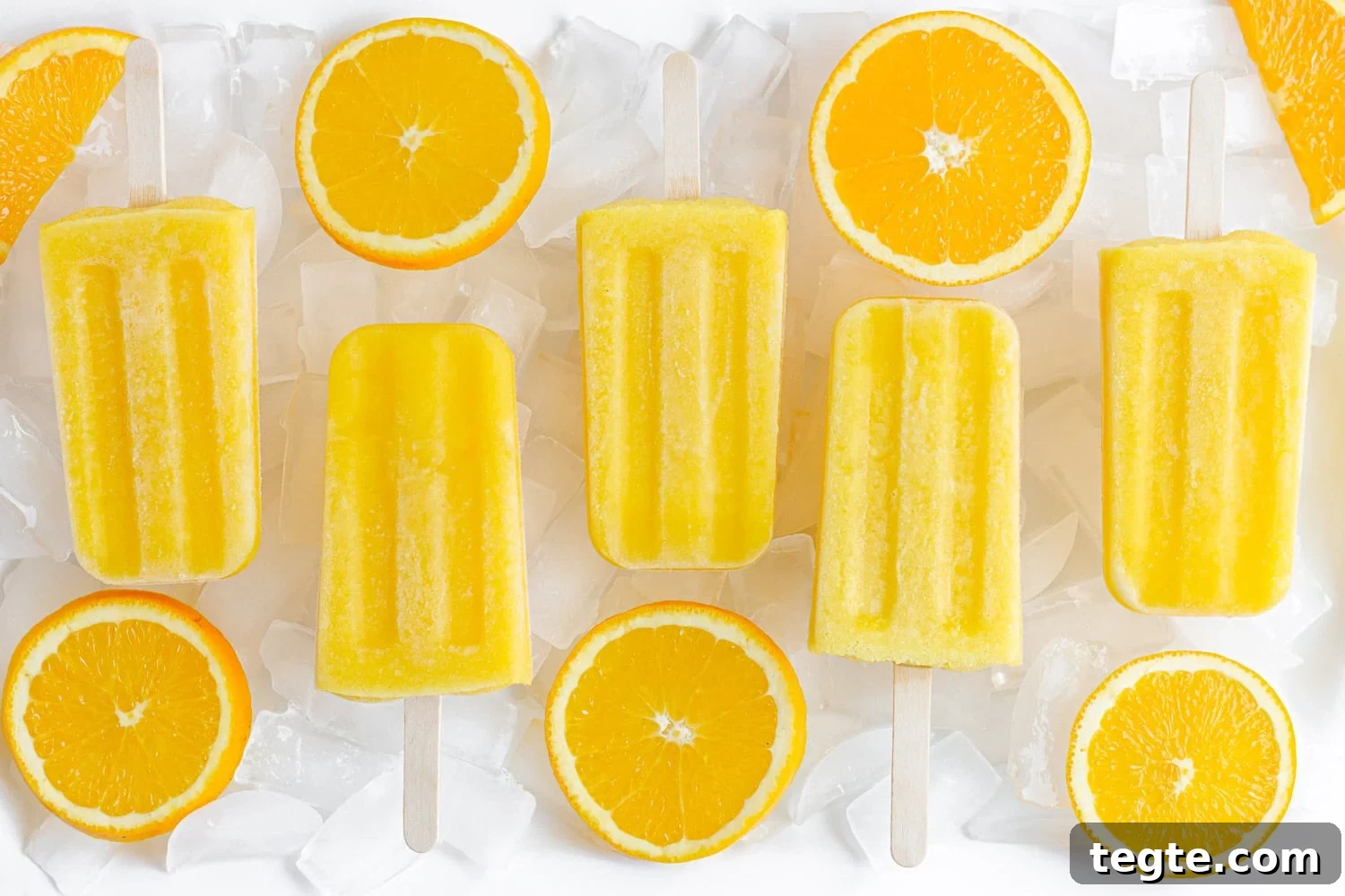 Refreshing Homemade Orange Popsicles Recipe 8 Orange popsicles lined up on a platter of ice with orange slices.
