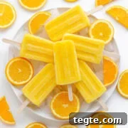 Plate of orange popsicles sitting on ice surrounded by sliced oranges.