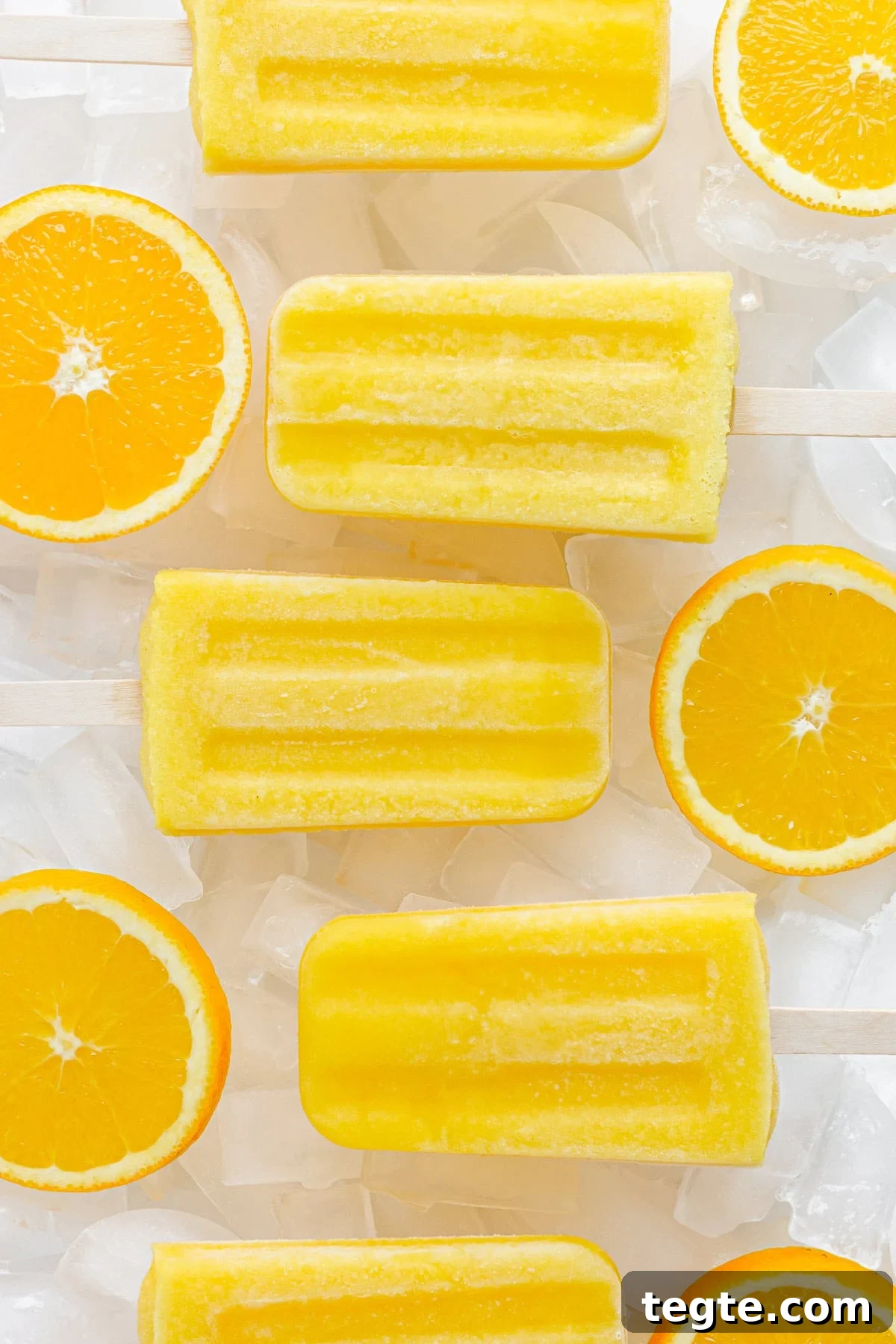 Refreshing Homemade Orange Popsicles Recipe 6 Overhead of homemade orange popsicles sitting on ice cubes with orange slices in between.