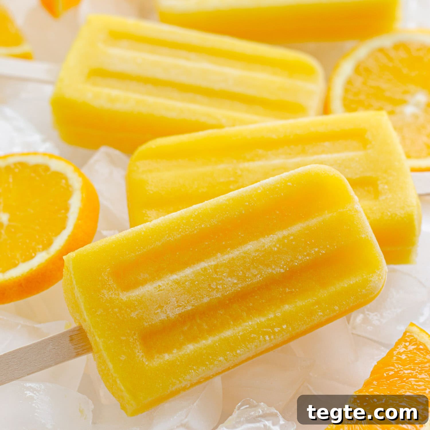 Refreshing Homemade Orange Popsicles Recipe 7 Orange popsicles sitting on ice with orange slices.
