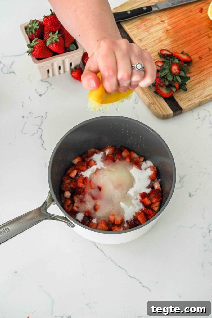 Homemade Small-Batch Strawberry Jam Recipe for Fresh Preserves 5 A hand squeezes lemon juice into a pot with diced strawberries and sugar.