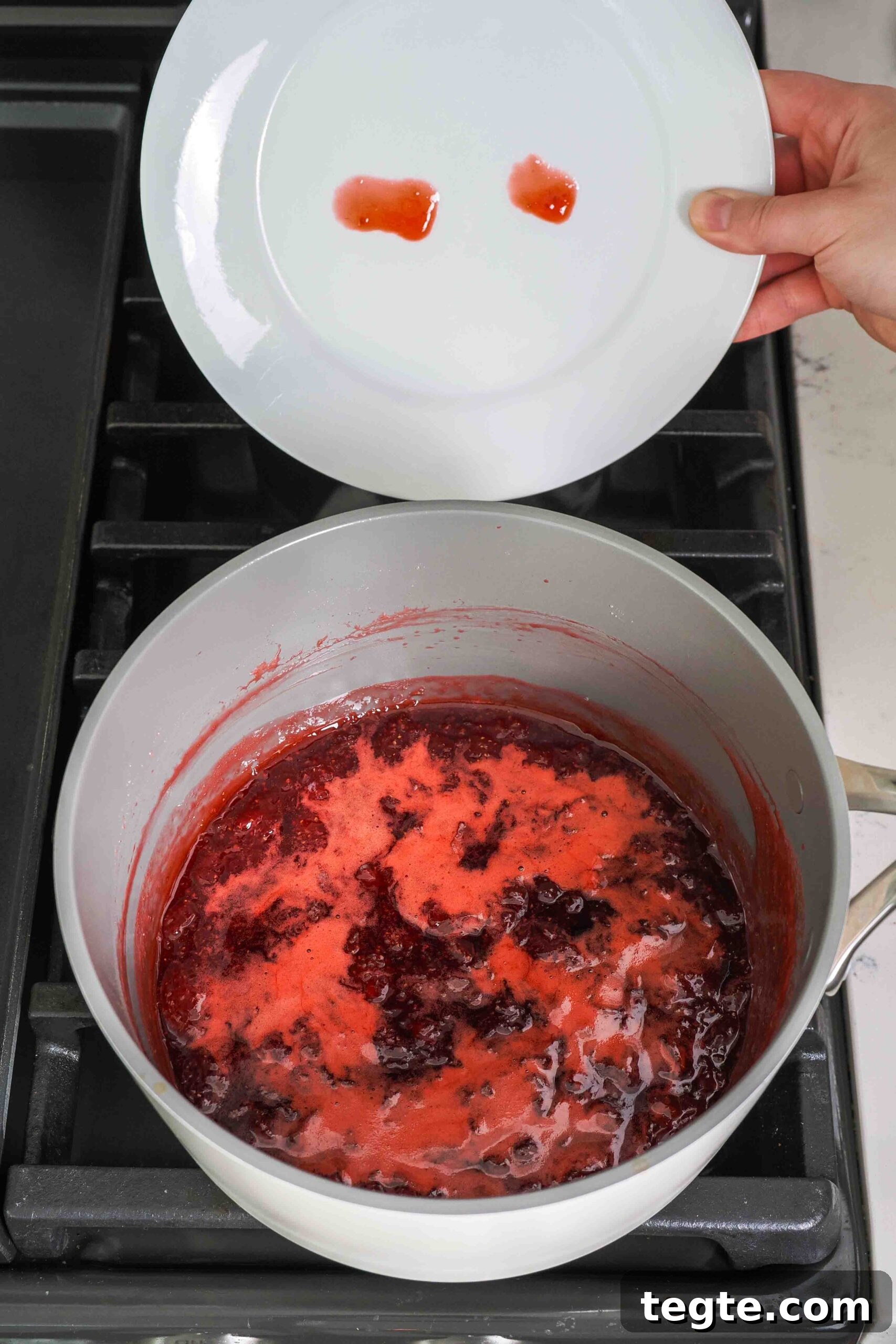 Homemade Small-Batch Strawberry Jam Recipe for Fresh Preserves 9 A plate with two dots of strawberry jam on it above a pot of strawberry jam. One dot is runny; the other is more circular.