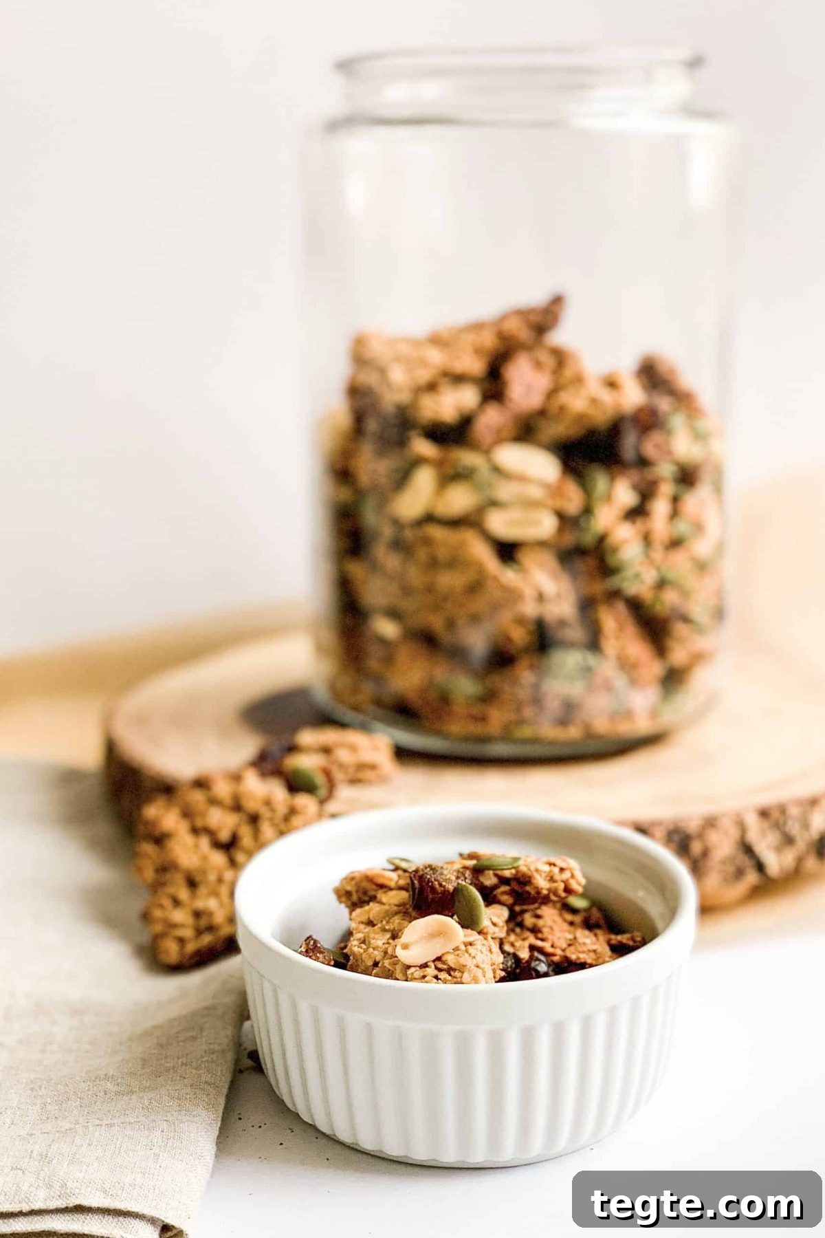 Crunchy Peanut Butter Granola Clusters Jar of crunchy peanut butter granola with peanuts, pepitas and chopped dates, sitting on decorative wooden platter