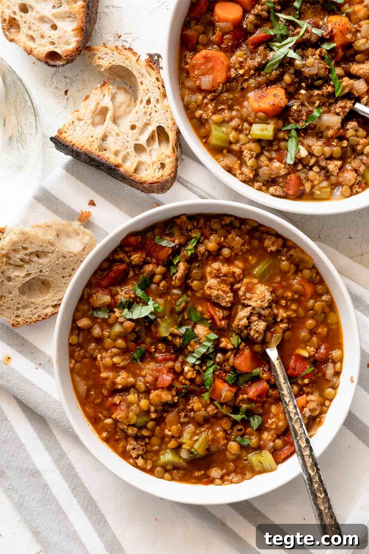 two bowls of lentil turkey soup with bread on the side