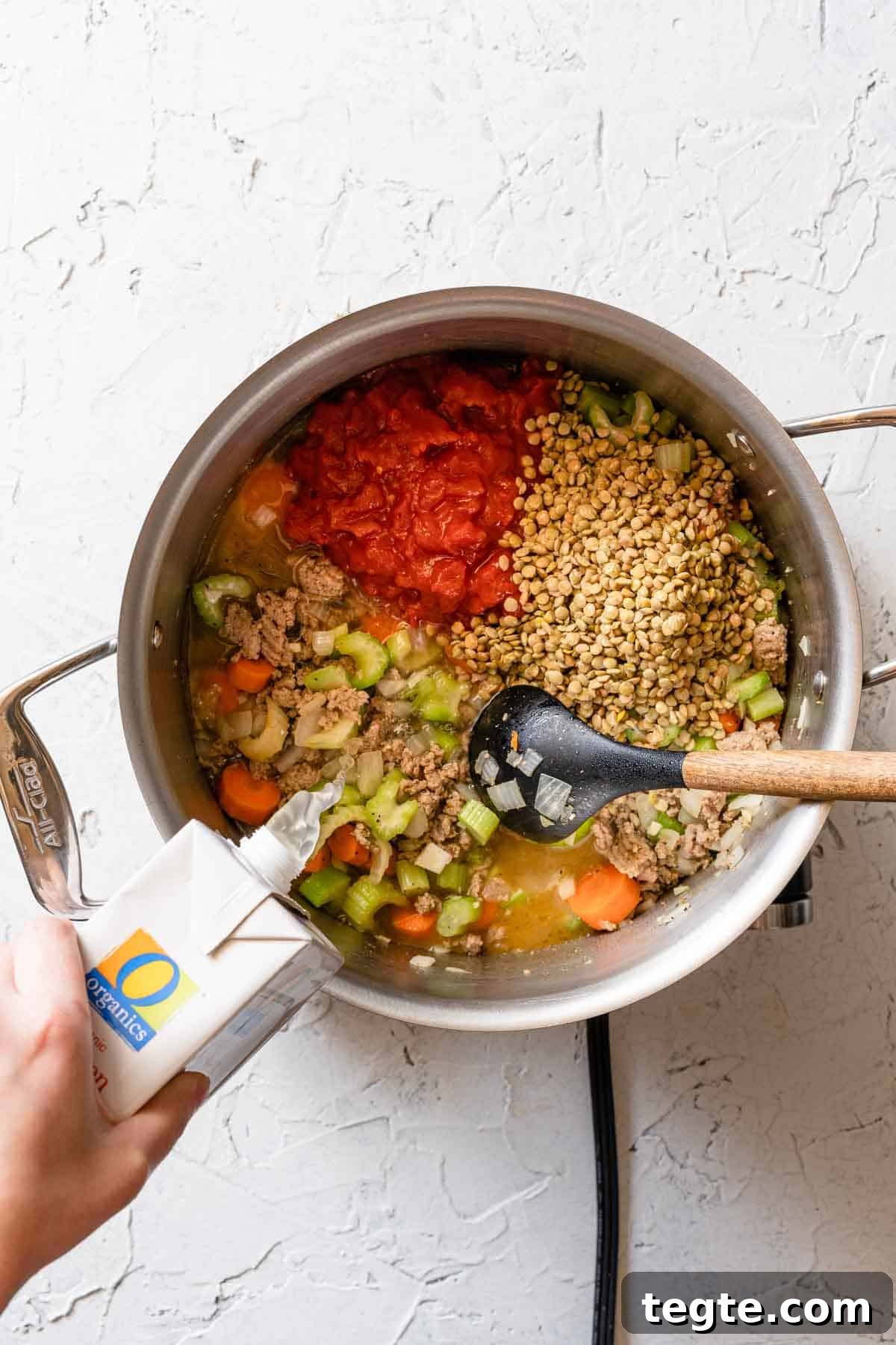 broth being poured into soup pot with lentils, turkey and veggies inside