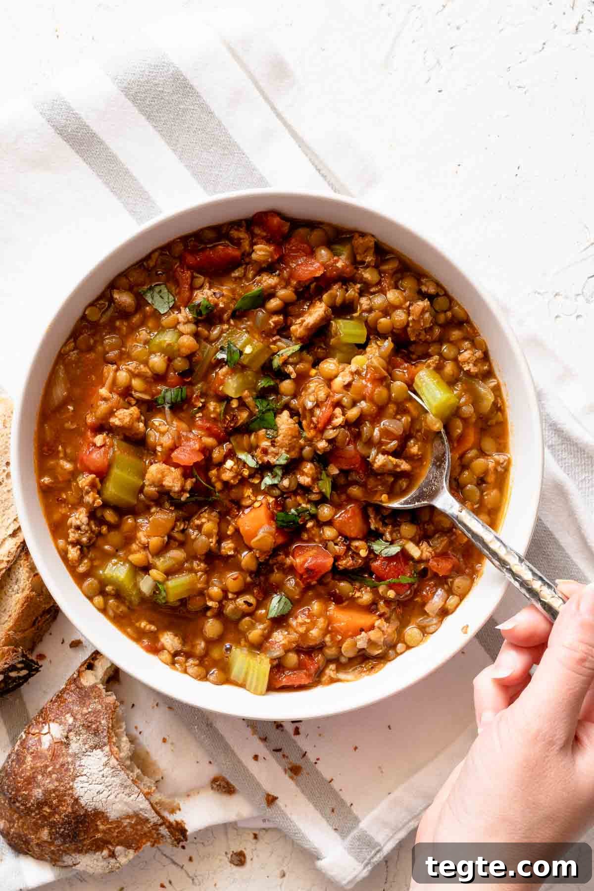 hand holding spoon scooping lentil turkey soup from bowl