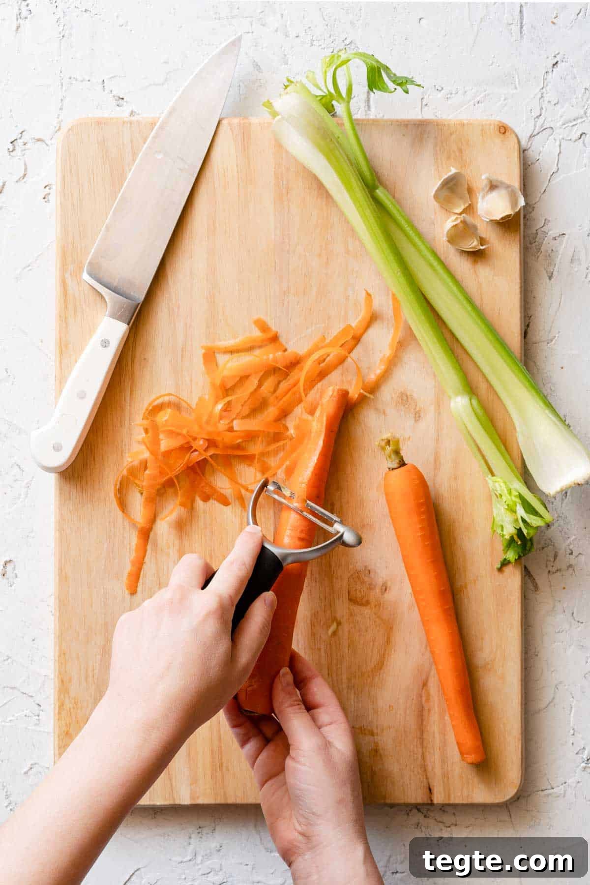 carrots being peeled on cutting board with celery and knife on the side