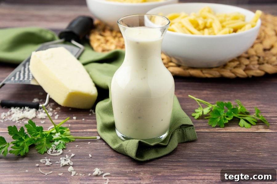 Creamy Asiago Sauce for Pasta and Vegetables 2 a glass carafe of white cheese sauce in front of a bowl of pasta