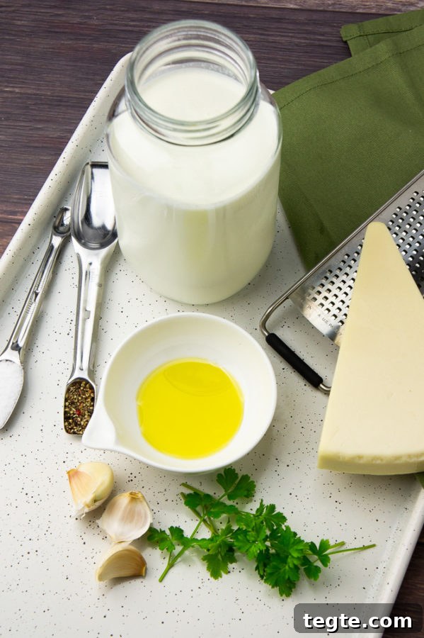 Creamy Asiago Sauce for Pasta and Vegetables 3 a jar of milk, wedge of asiago cheese, a bowl of oil, chopped parsley, and spices on a metal baking sheet
