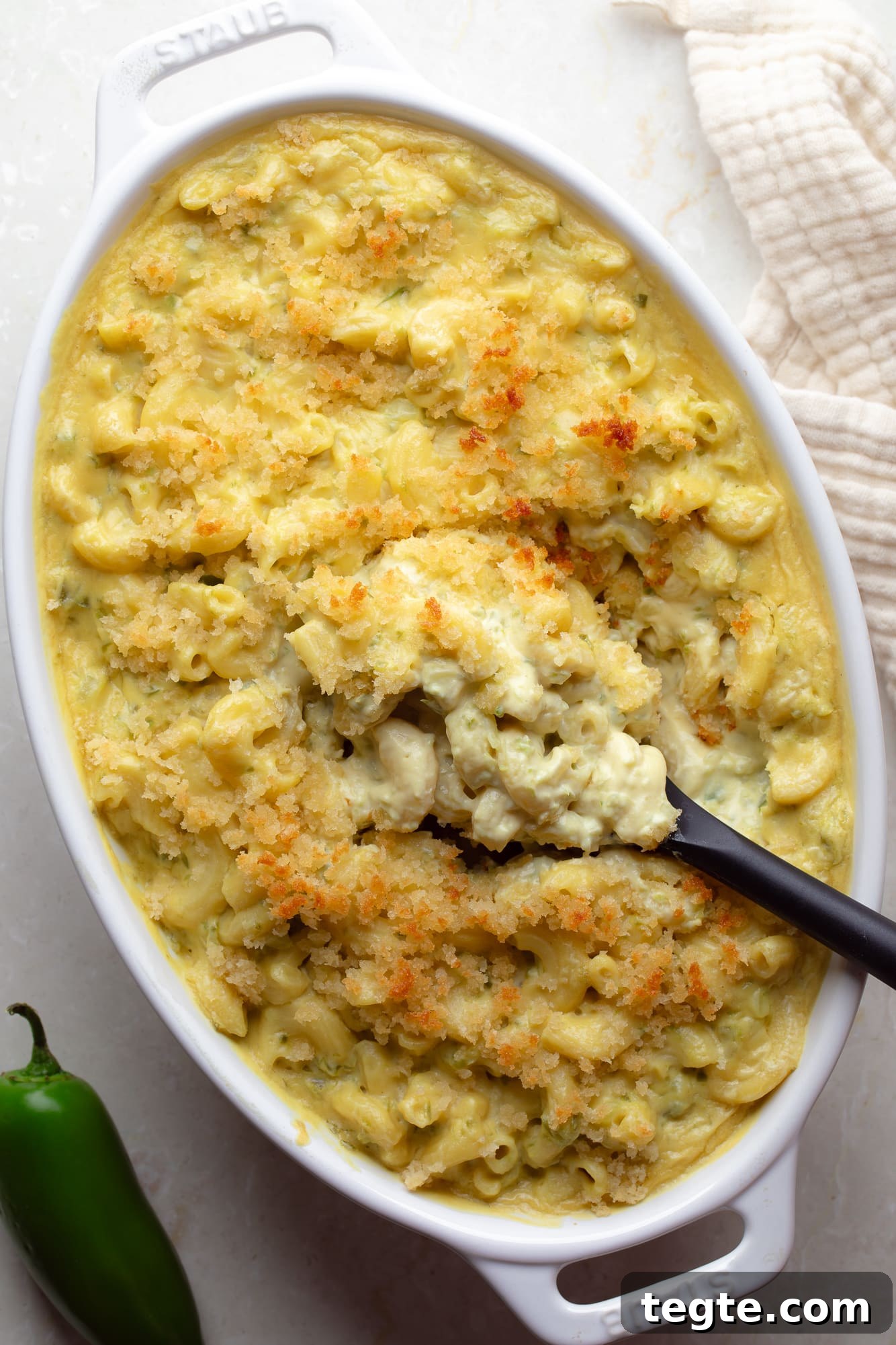Creamy Vegan Jalapeño Mac and Cheese Recipe 2 overhead view of a black spoon lifting a scoop of Vegan Jalapeño Mac and Cheese from a casserole dish.