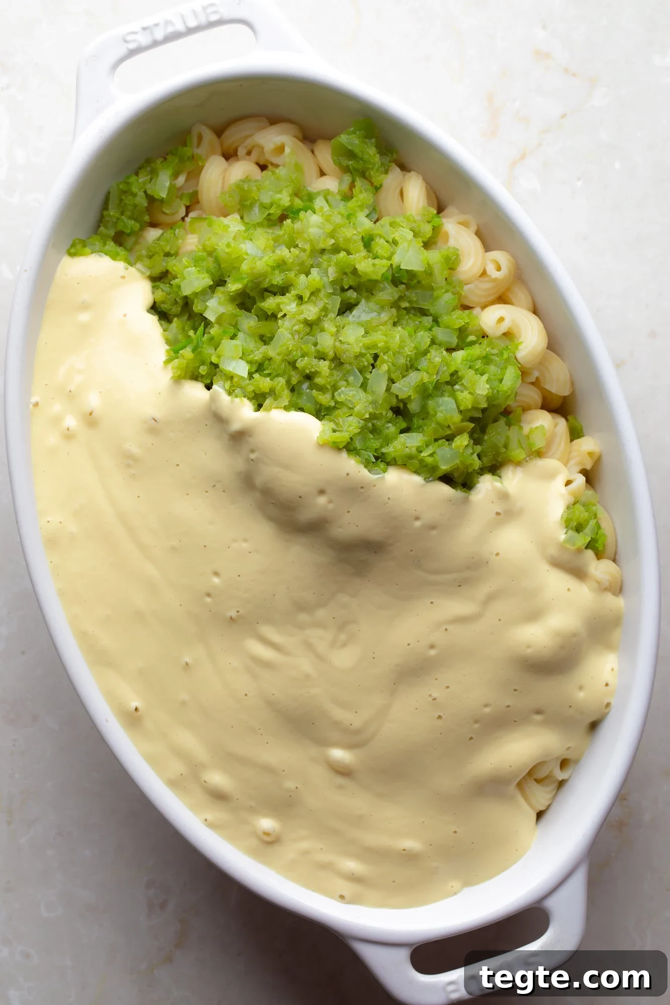 Creamy Vegan Jalapeño Mac and Cheese Recipe 5 overhead view of cashew cheese sauce, cooked jalapenos, and cooked pasta in a casserole dish.