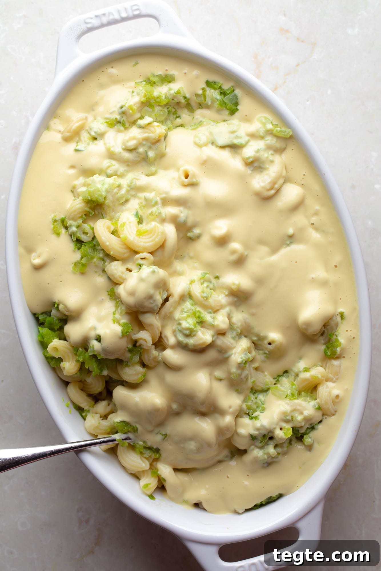 Creamy Vegan Jalapeño Mac and Cheese Recipe 6 overhead view of a spoon stirring vegan cheese sauce and pasta together in a casserole dish.