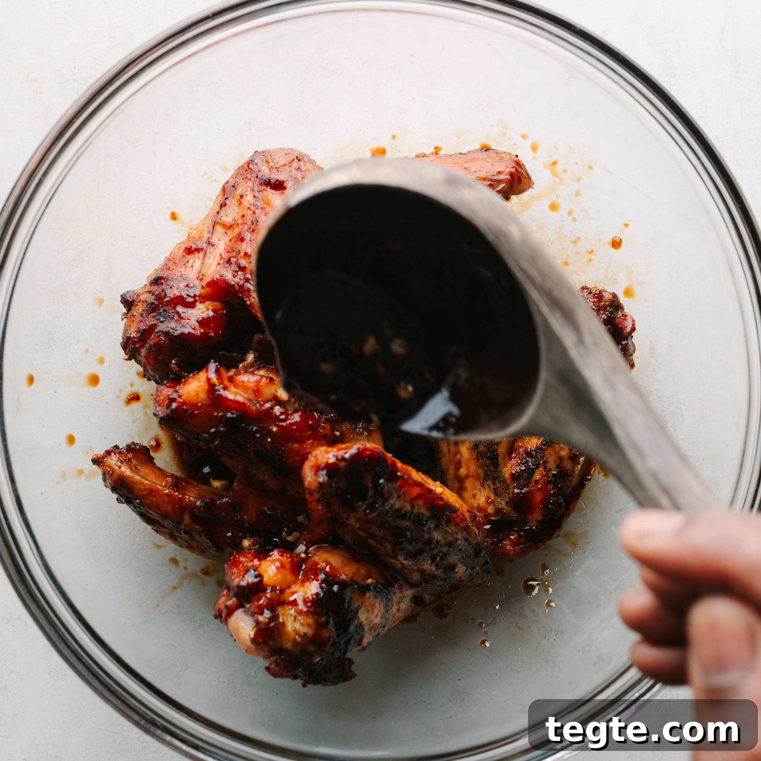 Asian Chili Garlic Chicken Wings Recipe 14 A clear glass bowl of Asian wings with Asian wing sauce being poured on top.