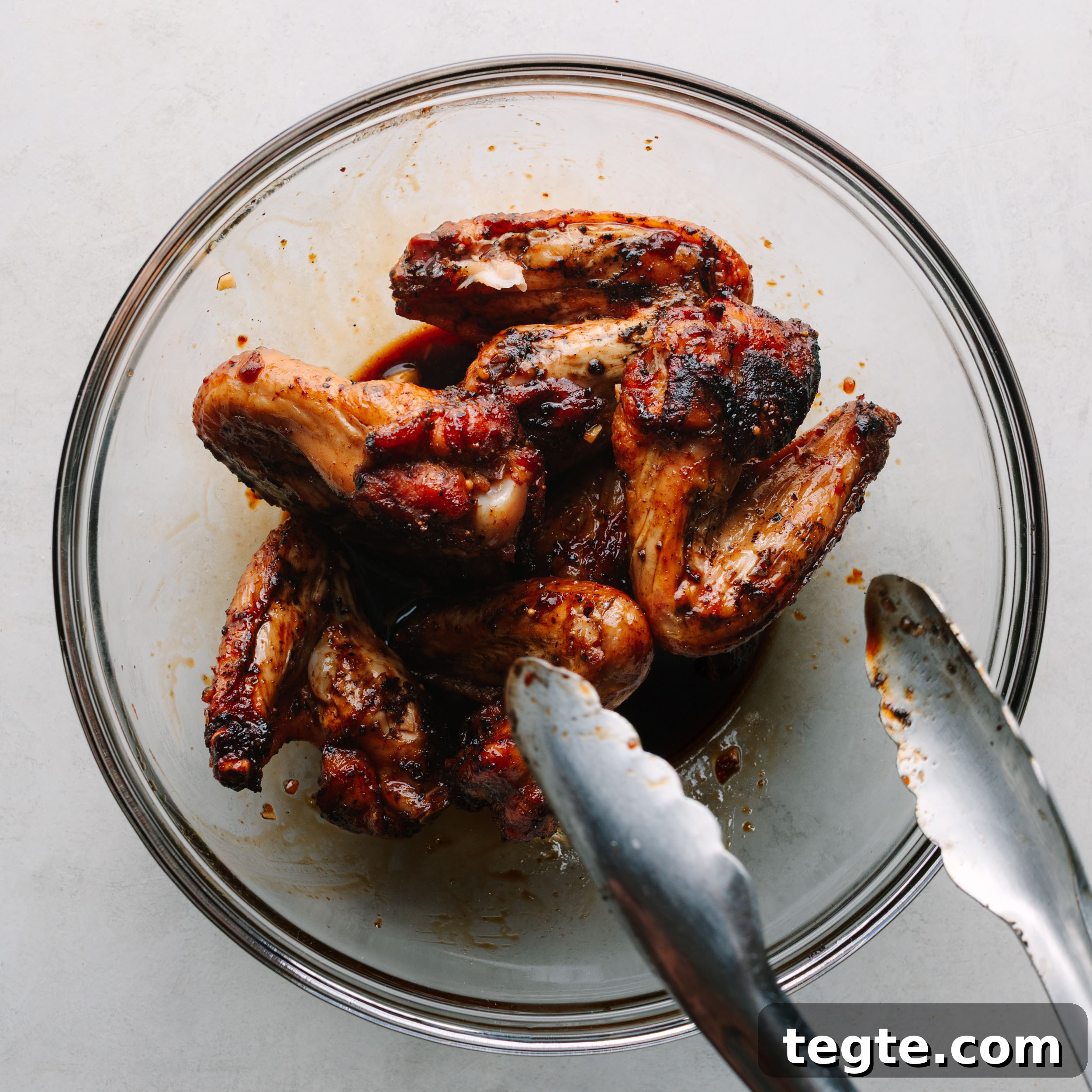 Asian Chili Garlic Chicken Wings Recipe 15 A clear glass bowl of Asian wings being tossed in Asian wing sauce.