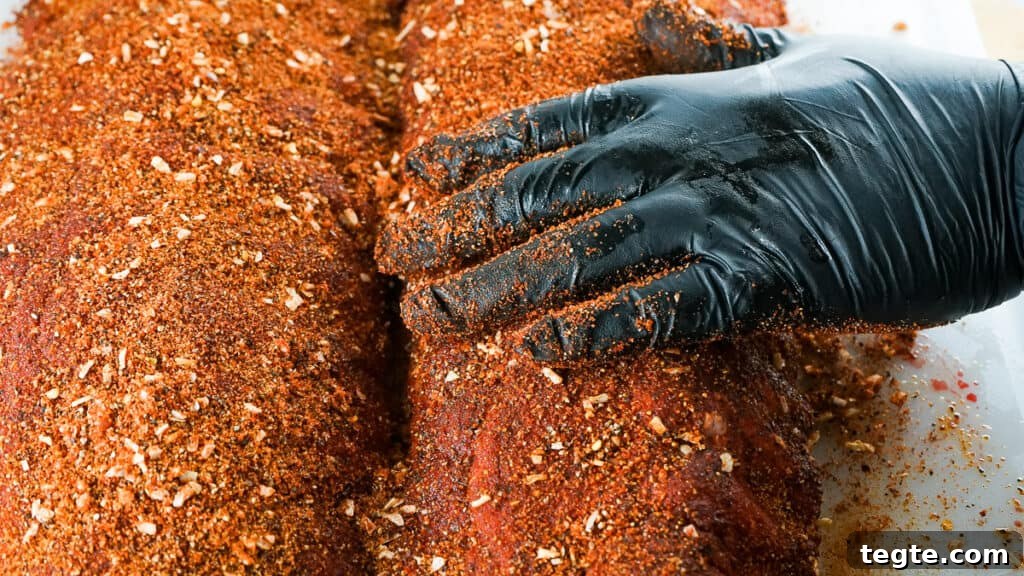 Gloved hand spreading rub all over baby back ribs